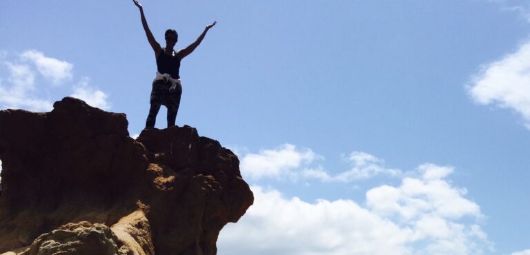 Person on the edge of a cliff with their hands up.